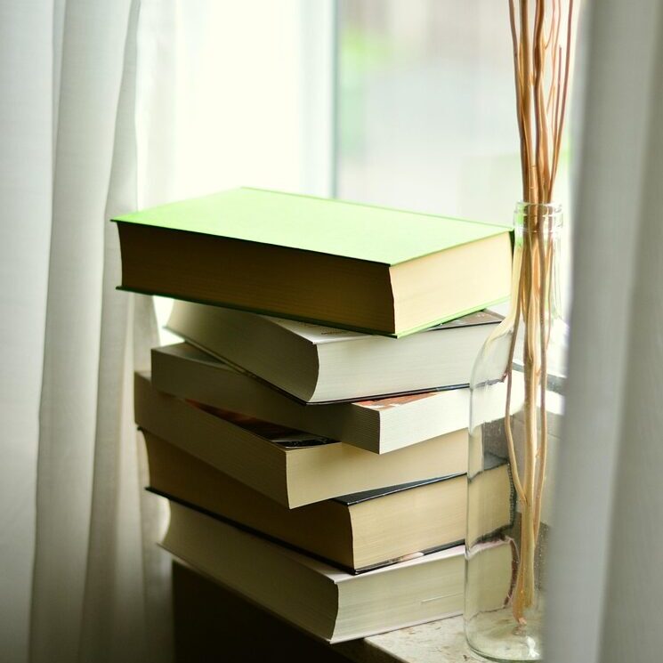A stack of books perched on a windowsill.
